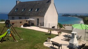 A house with a sloped roof, a patio with outdoor furniture, and a view of the sea.