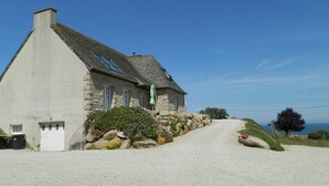 A stone building with a sloped roof, a gravel driveway, and a view of the sea.