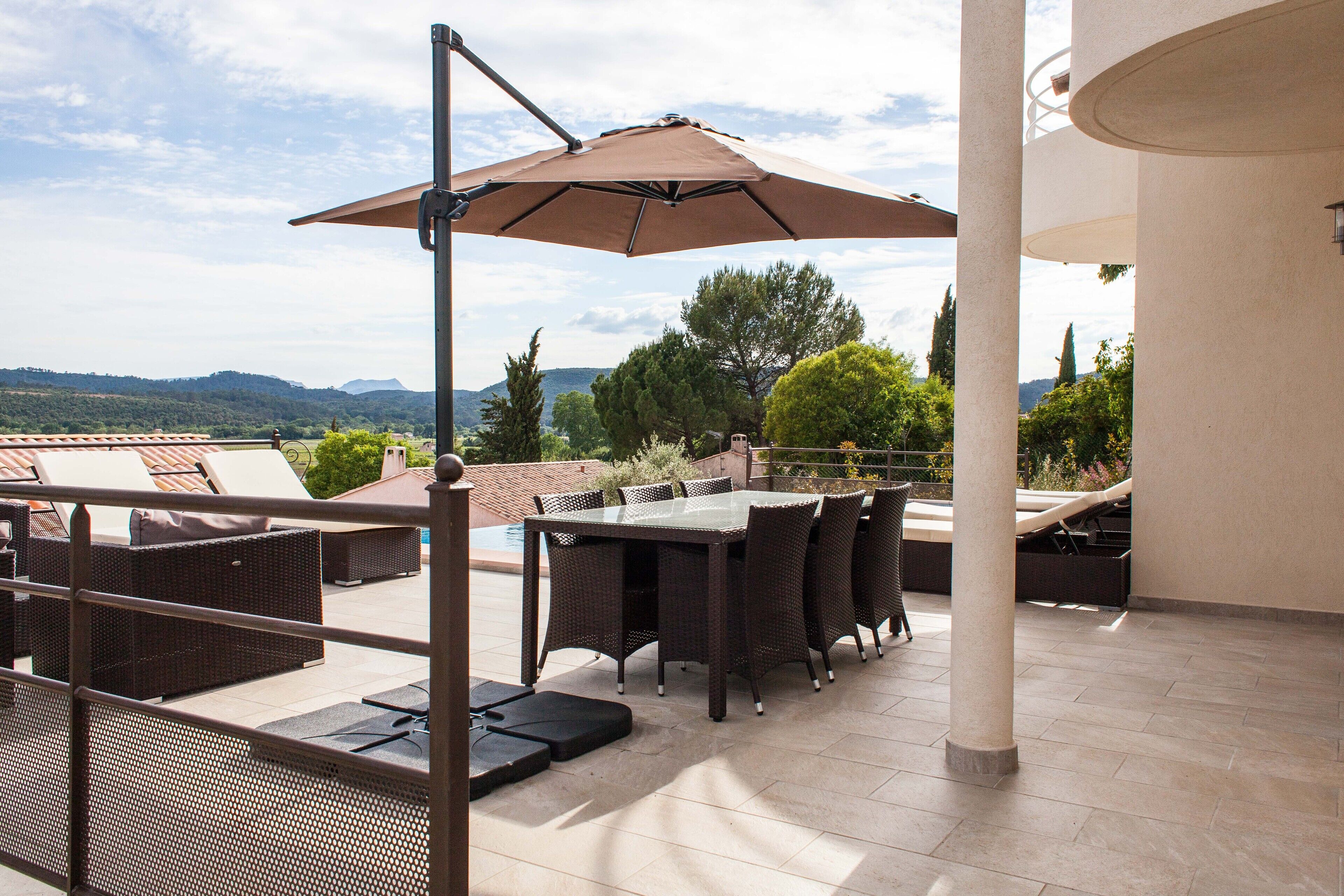 An outdoor patio with a table and chairs, a large umbrella, and a view of the landscape.