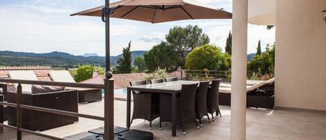 An outdoor patio with a table and chairs, a large umbrella, and a view of the landscape.