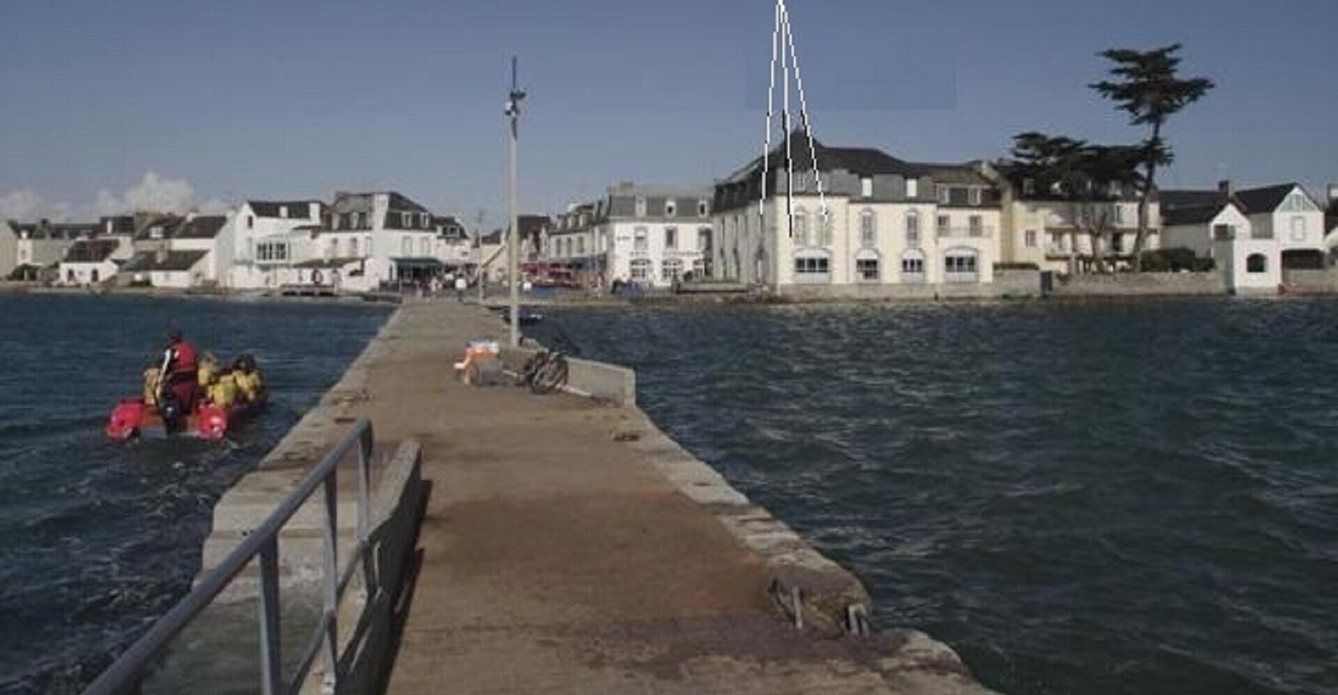 Une promenade en bord de mer, avec des bâtiments sur la gauche et une jetée qui s’avance dans l’eau.