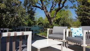 An outdoor seating area with a white table, grey sofa, and blue chairs.