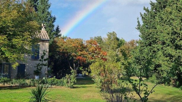A house with a garden, a visible rainbow, and a clear sky.