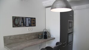 A kitchen with a wooden shelf, two black chairs, a hanging light fixture, and a microwave.