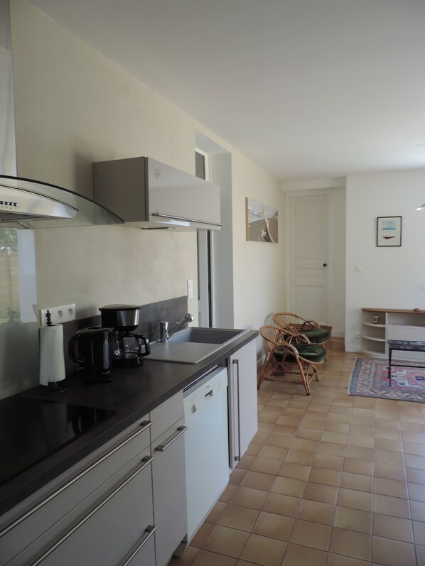 A compact kitchen with a built-in dishwasher, a coffee maker, and a sink. There is a dining area with a chair and a small table.