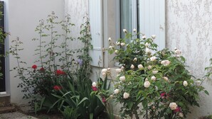 Een wit gebouw met een deur en raam, omringd door verschillende planten en bloemen.