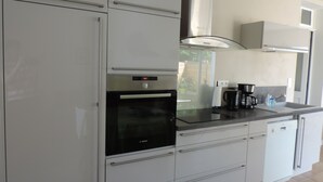 Een moderne keuken met witte kasten, een Bosch oven, een koffiezetapparaat en een vaatwasser.