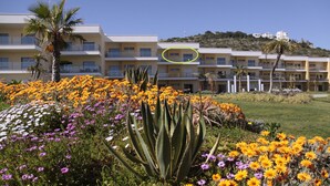 A hotel with multiple balconies, a landscaped garden with various flowers, and a hillside in the background. - Superb Albufeira apartment in the Algarve (la Marina Albufeira)