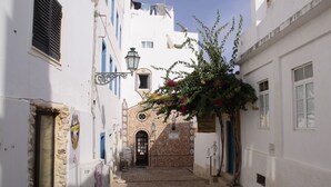 A narrow cobblestone street with white buildings, a stone archway, and a hanging flower arrangement. - Superb Albufeira apartment in the Algarve (la Marina Albufeira)