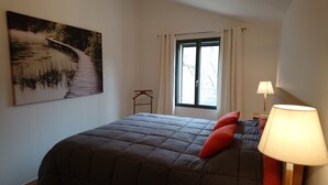 Een slaapkamer met een bed, een raam met gordijnen, een nachtkastje met een lamp en een schilderij aan de muur.