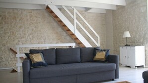 Un salon avec un canapé gris, un escalier en bois, un meuble blanc et une lampe.