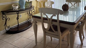 A dining area with a glass-top table, white chairs, a decorative vase, and a painting on the wall. - 4 BEDROOM HOUSE JUST A WALK TO THE BEACH! (Indian Harbour Beach)