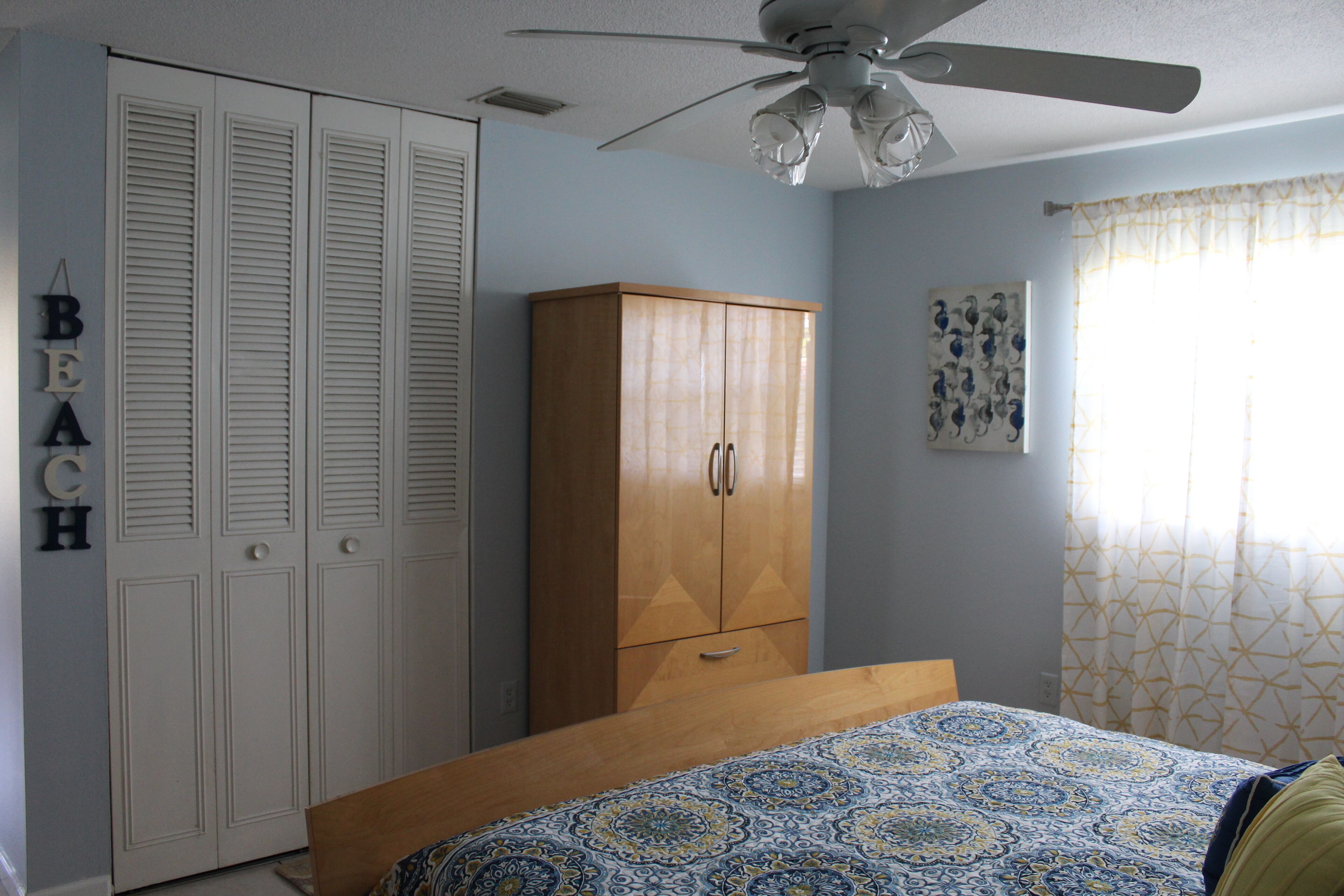 A bedroom with a bed, wardrobe, ceiling fan, and a wall with a 'BEACH' sign.