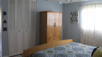 A bedroom with a bed, wardrobe, ceiling fan, and a wall with a 'BEACH' sign.