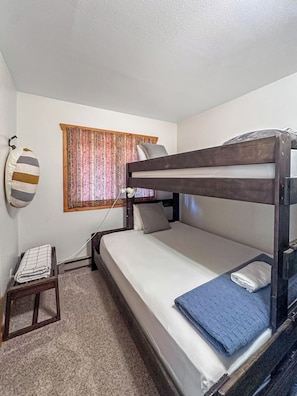 A bunk bed with a wooden frame, a small bedside table, and a power outlet.