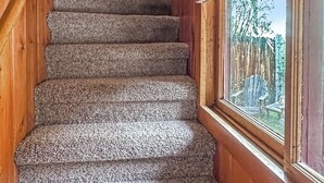 A wooden interior with a carpeted staircase leading to a window overlooking a wooden deck.