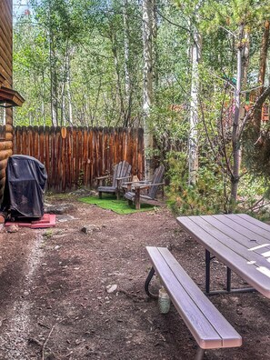 Eine Holzterrasse mit Picknicktisch und Stühlen, umgeben von einem Holzzaun und Bäumen.