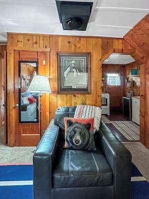 Ein Zimmer mit einer Ledersofa, einem gerahmten Bild, einer Lampe und einem Teddybär-Kissen.