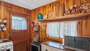 A compact kitchen with wooden walls, a white refrigerator, a stove, a microwave, and a small refrigerator.