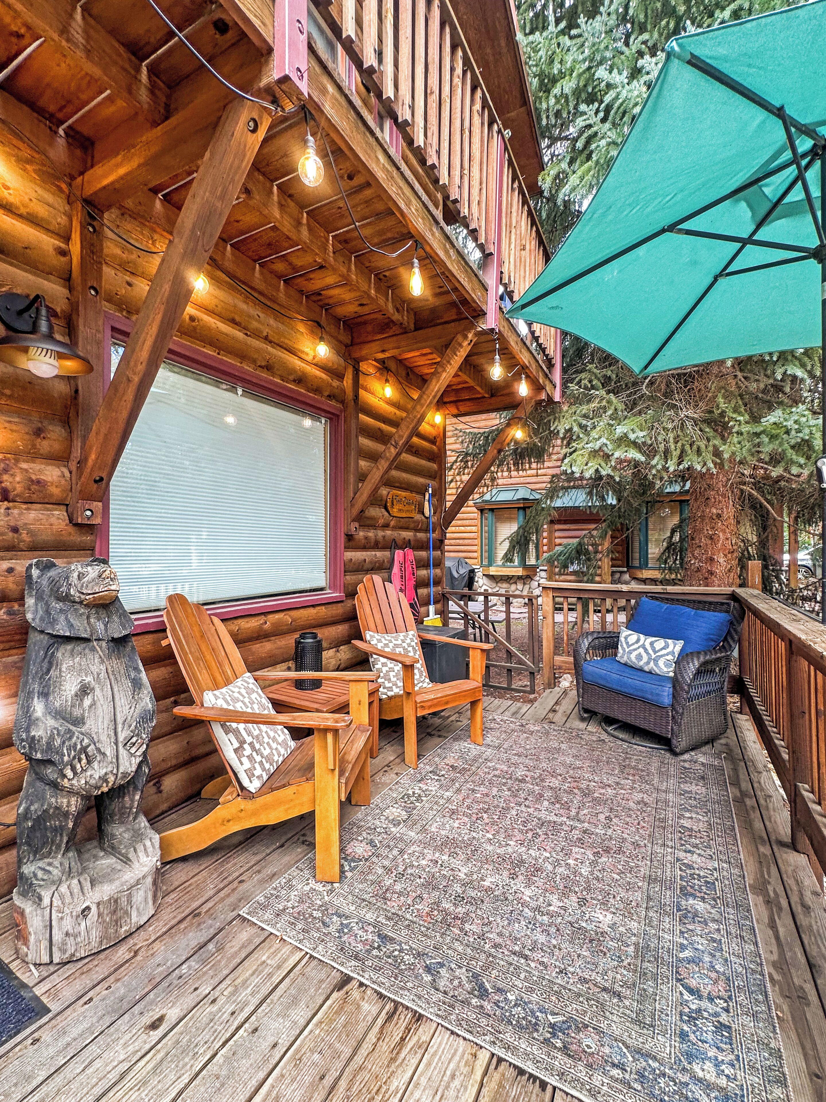 A wooden deck with outdoor seating, a stone bear sculpture, and a green umbrella.