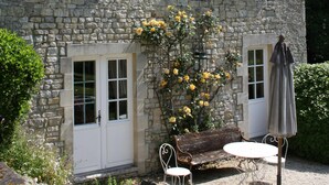A stone building with two windows, a door, a bench, and a table with an umbrella. - Charming house in the park of a historic monument castle (Barbeville)