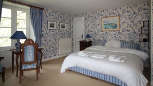 A bedroom with a large bed, a chair, a table, a lamp, a radiator, a door, and a painting on the wall. - Charming house in the park of a historic monument castle (Barbeville)
