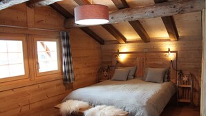 Ein Schlafzimmer in einer Holzhütte mit einem Bett, zwei Nachttischlampen und einem Fenster mit Vorhängen.