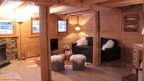 Ein gemütliches Blockhaus-Interieur mit Kamin, Fernseher, einer Couch und einer Lampe.