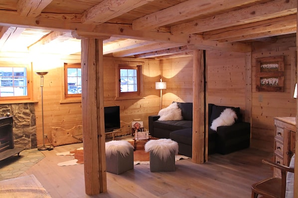 A cozy log cabin interior with a fireplace, a television, a sofa, and a lamp.