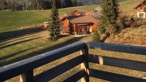 Eine hölzerne Bank mit Blick auf eine Berglandschaft, im Vordergrund ein Chalet.
