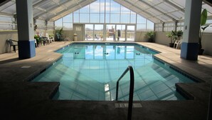 An indoor swimming pool with clear glass walls, a tiled floor, and a roof structure.