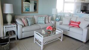 A living room with a white sofa, a glass coffee table, and a wicker side table.