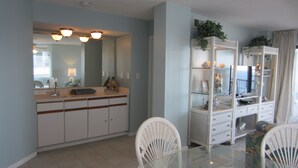 A modern kitchen with white cabinetry, a glass dining table, and white wicker chairs.