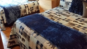 Ein gemütliches Schlafzimmer in einer Holzhütte mit zwei Betten, Holzwänden und einem Deckenventilator.