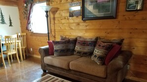 Ein Holzinterieur mit einer Couch, gemusterten Kissen, einem Teppich und einem 'Welcome'-Schild.