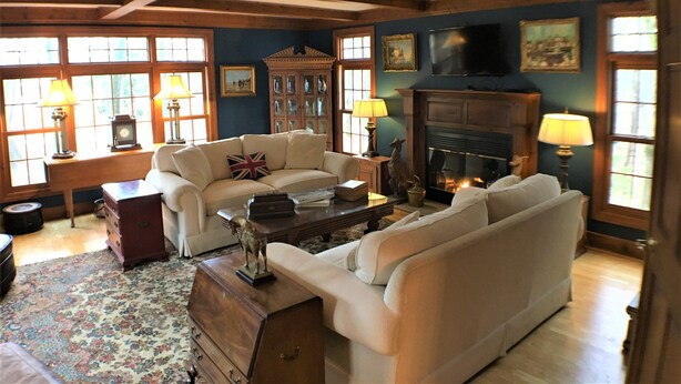 A traditional living room with a fireplace, wooden beams, and a classic fireplace mantel.