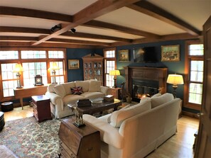 A traditional living room with a fireplace, wooden beams, and a classic fireplace mantel.