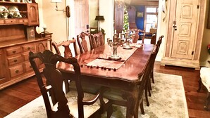 A dining room with a long wooden table, multiple chairs, a chandelier, and a Christmas tree.