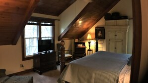 A bedroom with a large bed, a dresser, a chair, a lamp, and a television.
