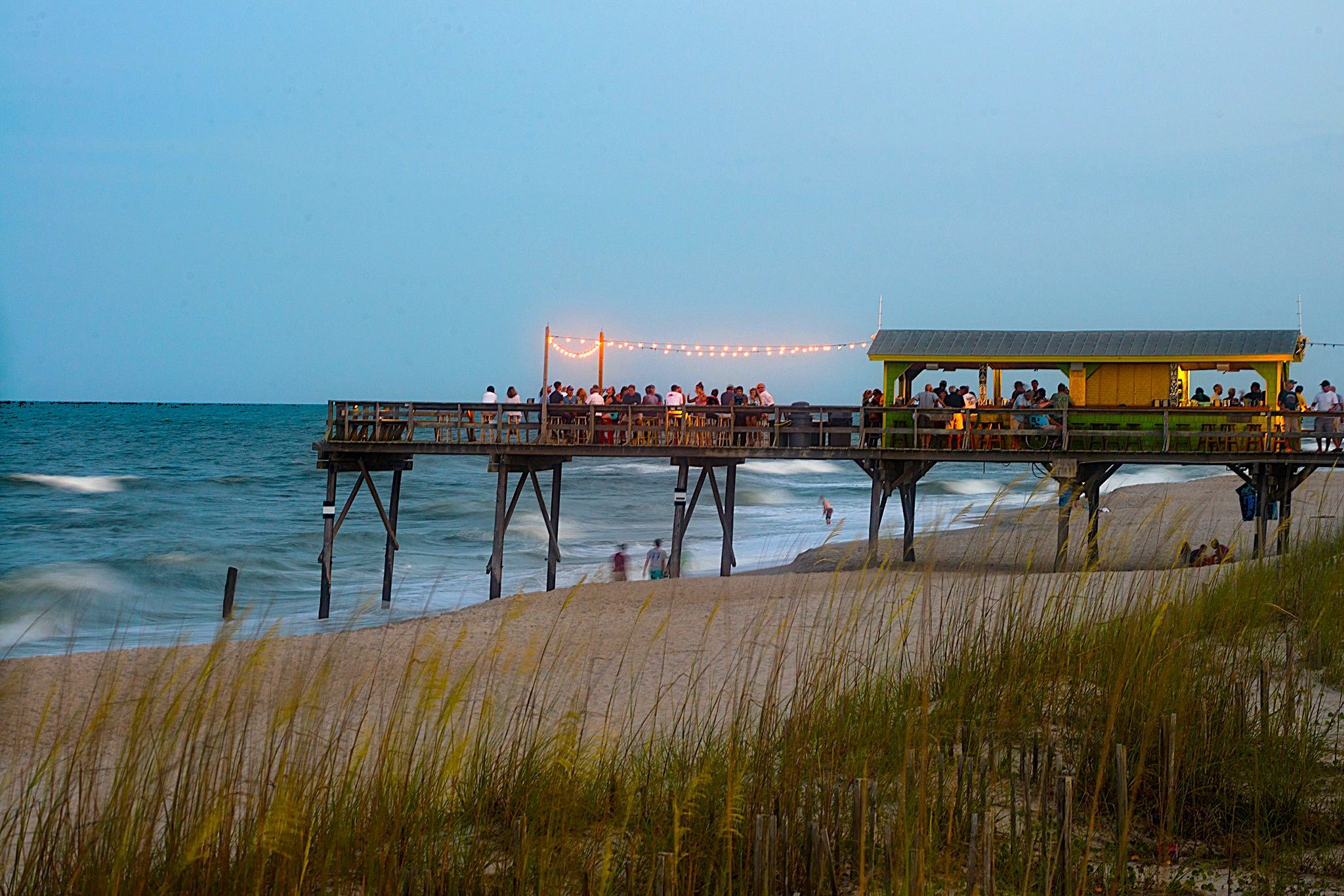 A pier with a restaurant on it, overlooking the beach and ocean.