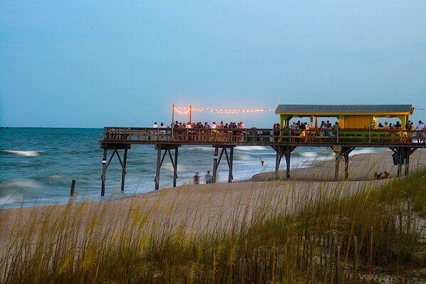 A pier with a restaurant on it, overlooking the beach and ocean.