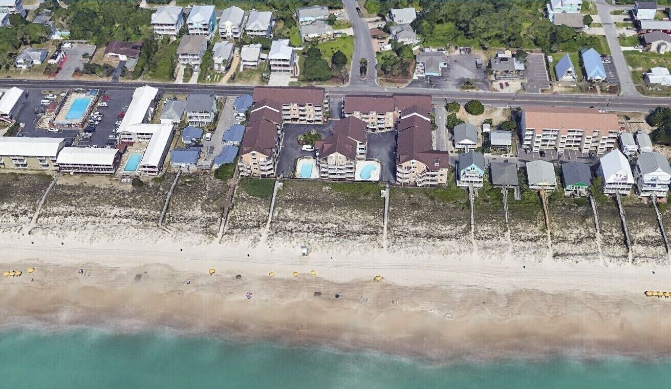 An aerial view of a coastal residential area with multiple apartment buildings, a beach, and a parking lot.