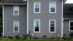 A two-story house with a symmetrical facade, multiple windows, and a well-maintained lawn with various plants and a statue.