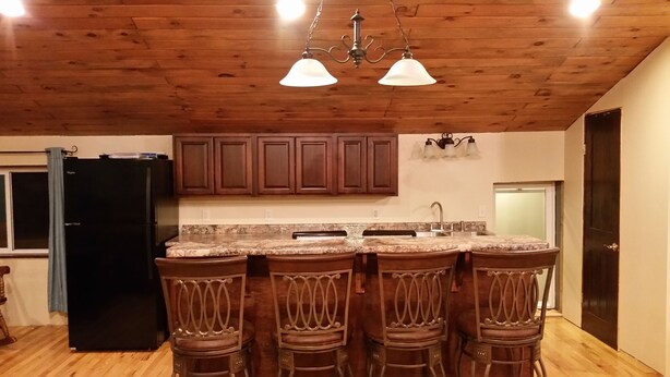 A kitchen with wooden cabinets, a black refrigerator, a granite countertop, and a bar area with four stools.