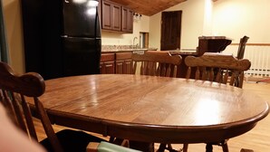 A wooden dining table surrounded by chairs in a kitchen with wooden cabinets and a black refrigerator.