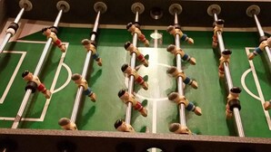 A foosball table with a green playing surface and metal rods with figures.