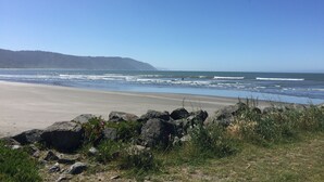 Una playa con un primer plano rocoso, una orilla arenosa y una colina boscosa al fondo.