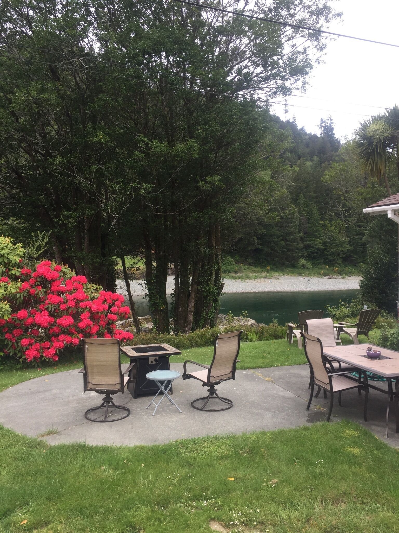 An outdoor patio with a table and chairs, surrounded by lush greenery and a view of a lake.