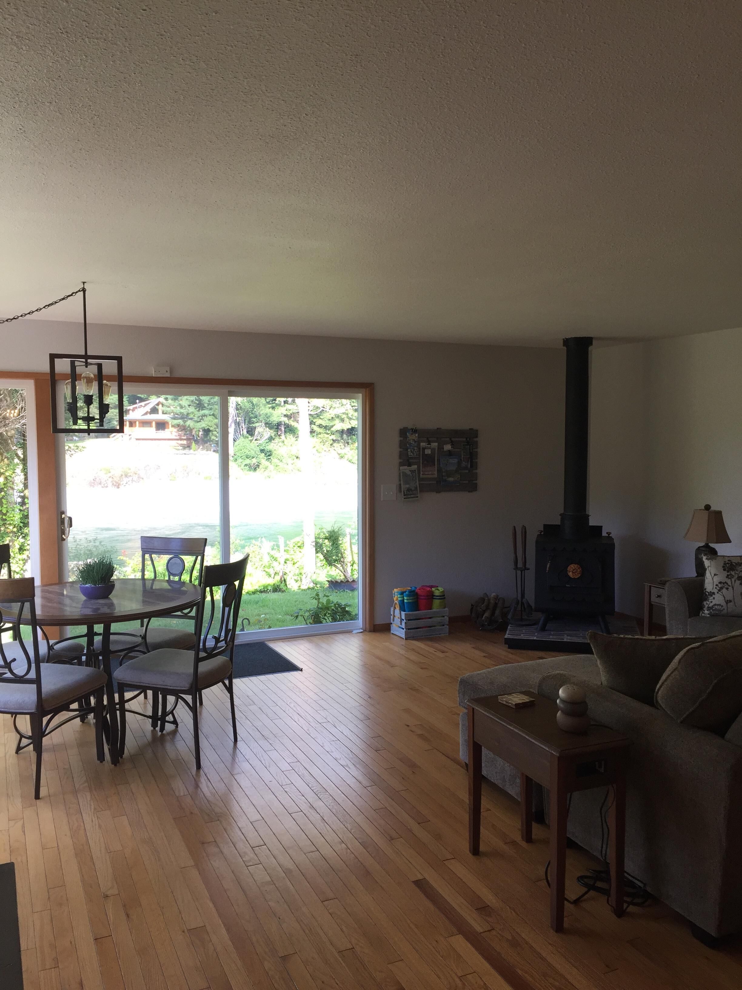 Ein Wohnzimmer mit Holzboden, einer Couch, einem Esstisch mit Stühlen, einem Kamin und Blick durch eine Glastür.