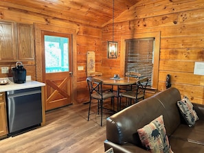 Interior de una cabaña de madera con comedor, sofá, refrigerador y puerta de madera.